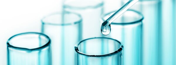 Close‑up of a dropper releasing a liquid into a row of clear glass test tubes.